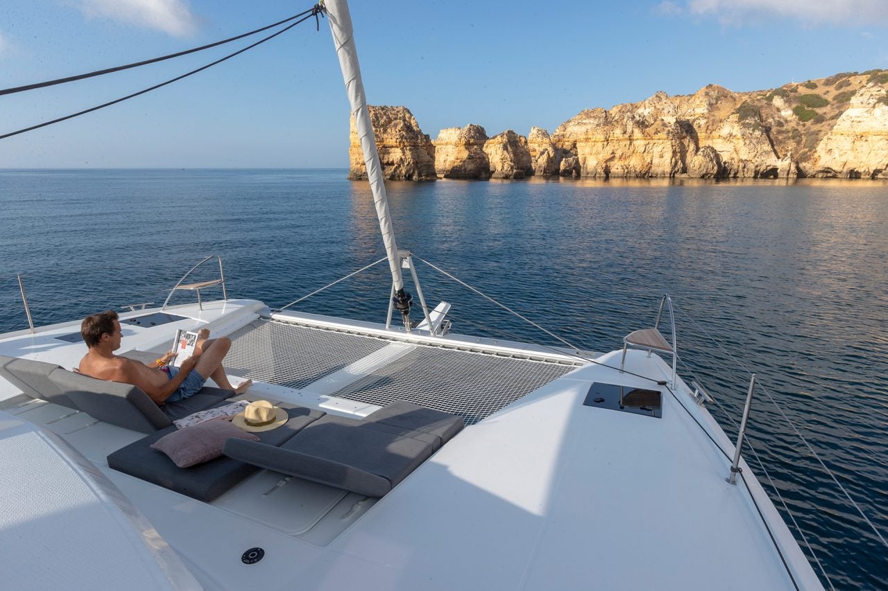 Ein Mann sitzt auf dem Vordeck des Segelkatamarans Fountaine Pajot Elba 45