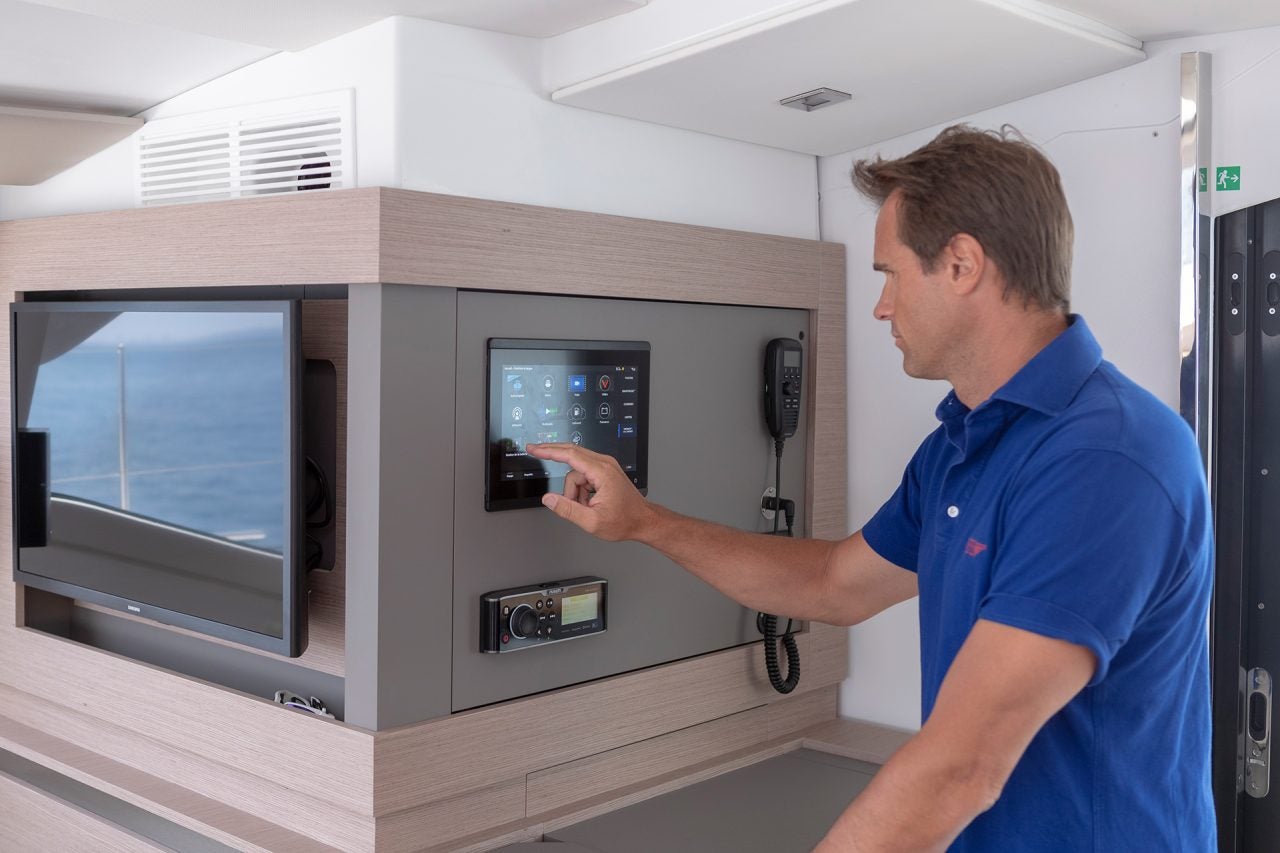 Un hombre usando un panel electrónico interior del catamarán Fountaine Pajot 67