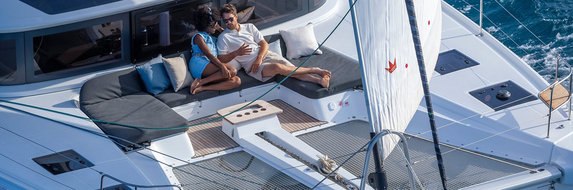 Pareja en la cubierta de proa del nuevo modelo de yate a vela catamarán en venta