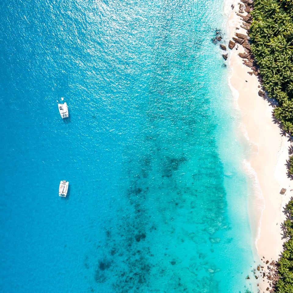 Vista aérea de playa de un destino isleño y de dos catamaranes a vela de Dream Yacht