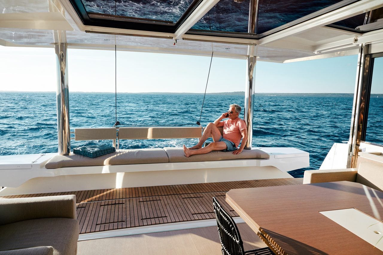 Homme assis sur une banquette du tableau arrière du catamaran à voile Bali 5.4 surplombant la mer