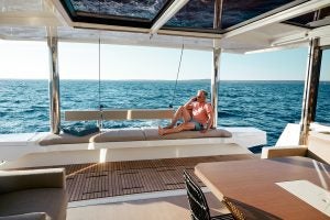 Homme assis sur une banquette du tableau arrière du catamaran à voile Bali 5.4 surplombant la mer