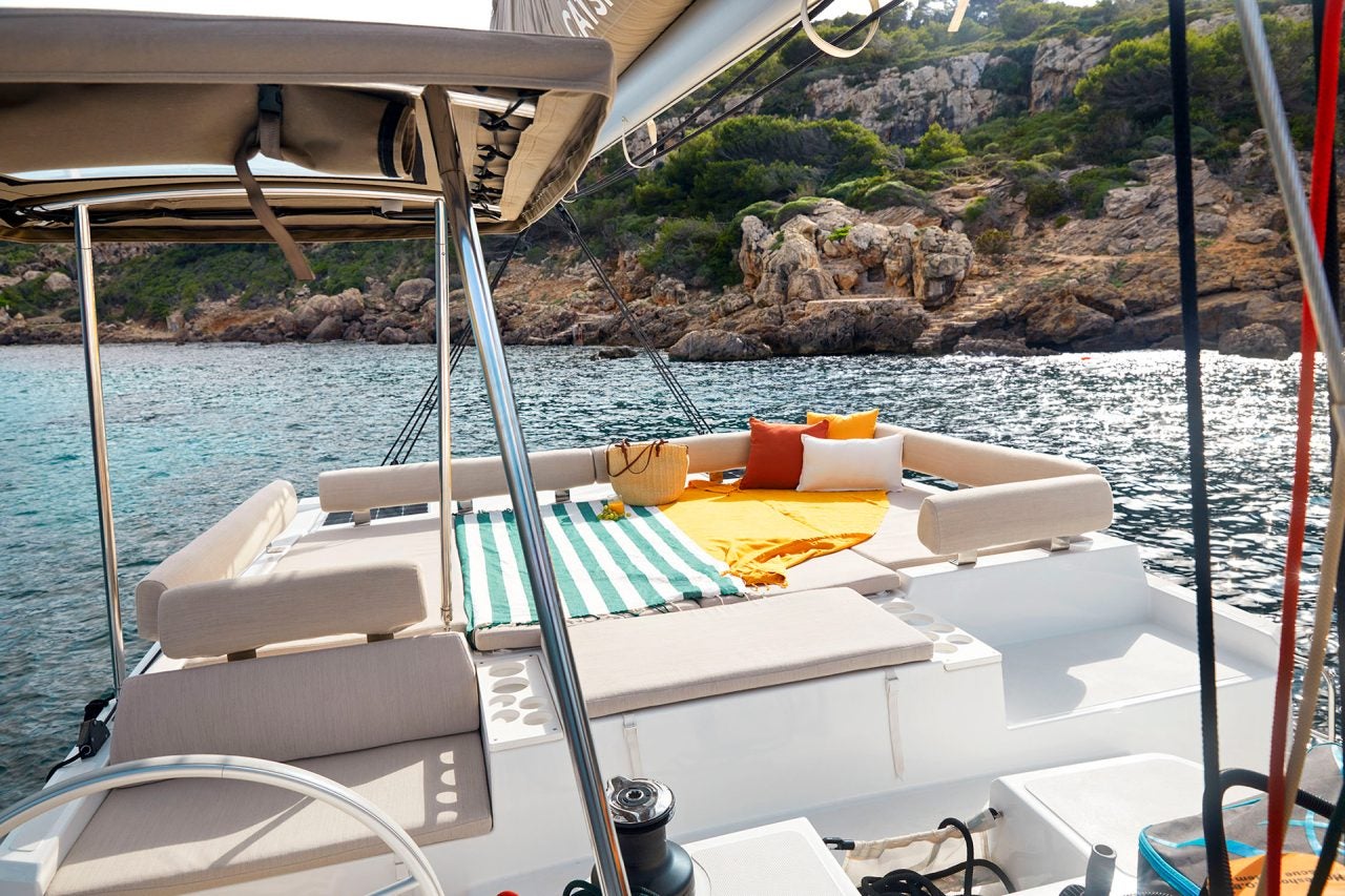 Salotto con lettini prendisole sul flybridge della barca a vela Bali Catspace con vista sul litorale e sul mare blu