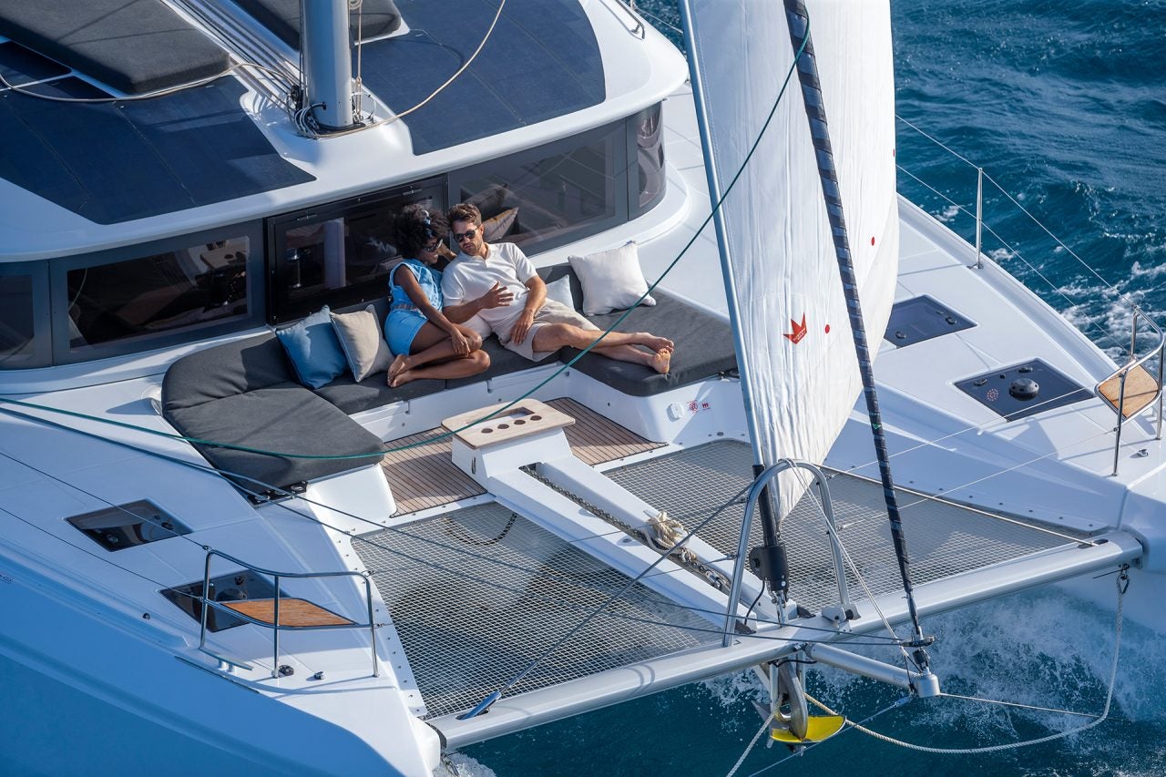 Pareja en la cubierta de proa del nuevo modelo de yate a vela catamarán en venta