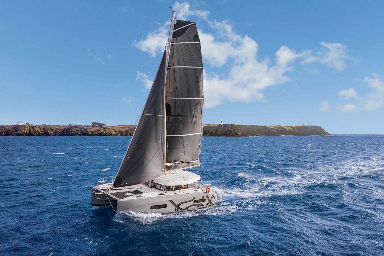 Catamarán Excess 11 a toda vela con una isla repleta de vegetación en la distancia