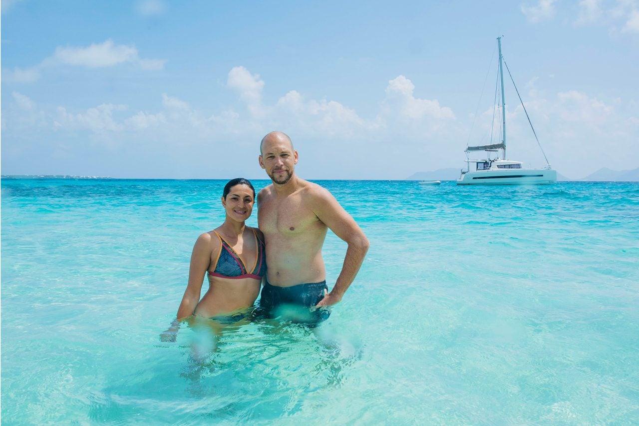 Ein Paar steht im blauen Wasser mit einem Dream-Yacht-Katamaran im Hintergrund