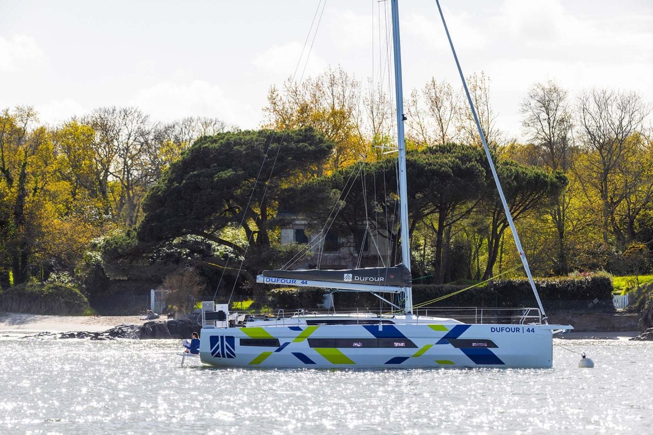 Vue latérale d’un monocoque à voile Dufour 44 ancré près d’un rivage pittoresque