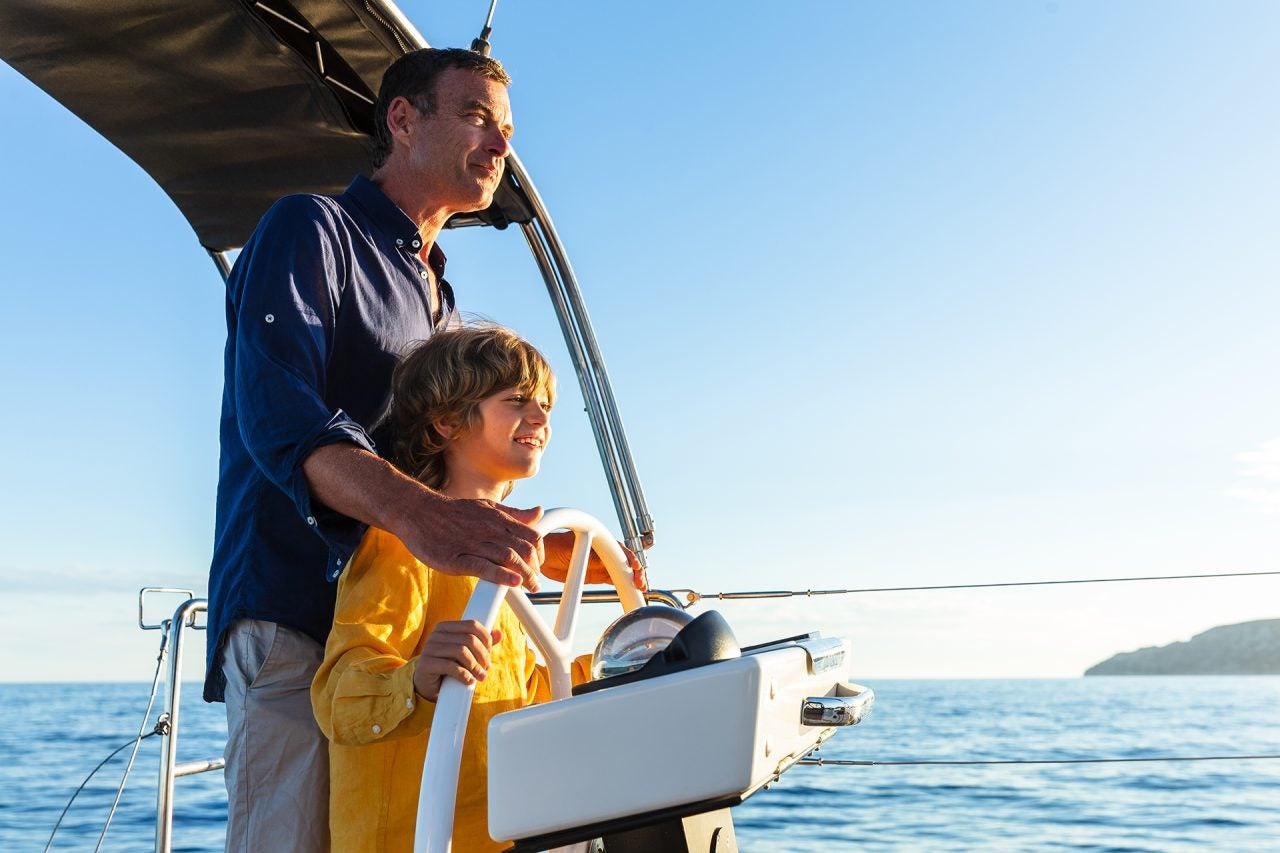 Hombre e hijo al timón de un velero monocasco modelo Dufour