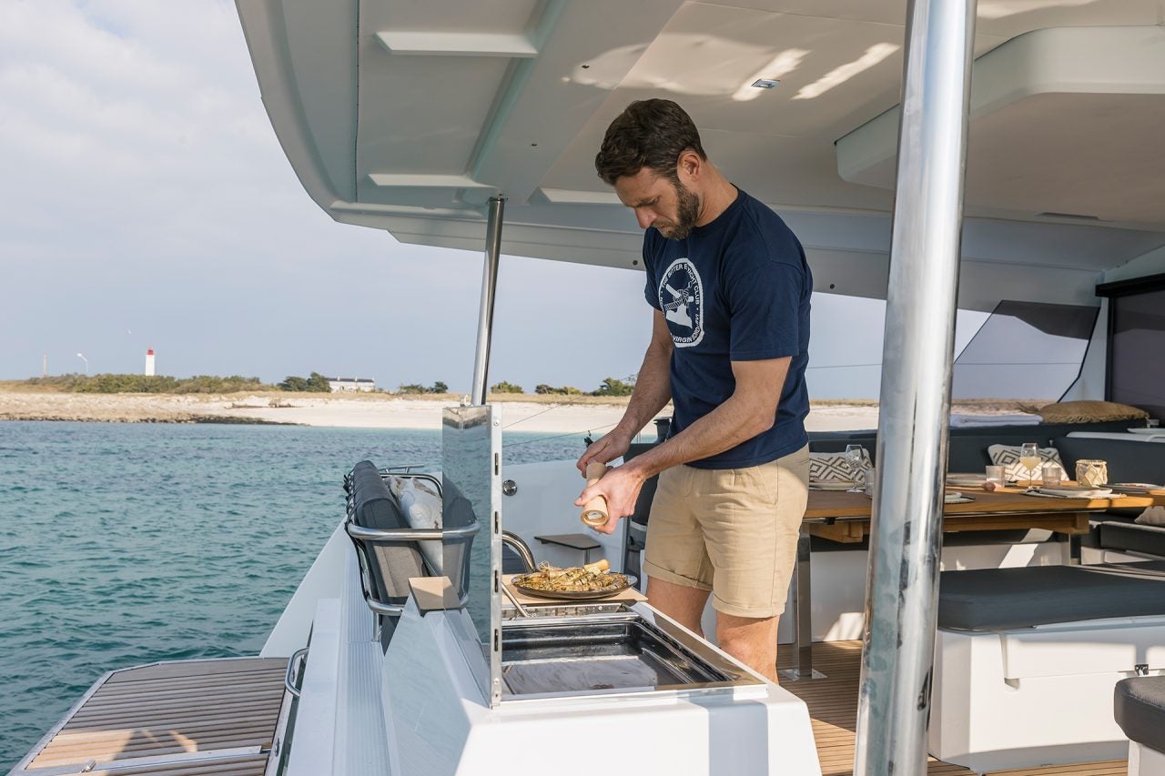 Ein Mann nutzt den Außengrill des Elektro-Katamarans Fountaine Pajot Aura 51