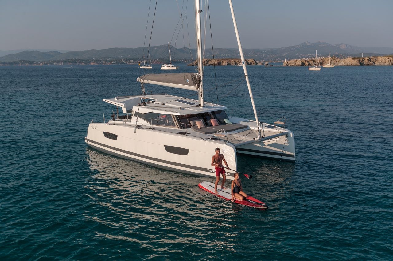 Homme faisant du paddlesurf à côté du catamaran à voile Isla 40