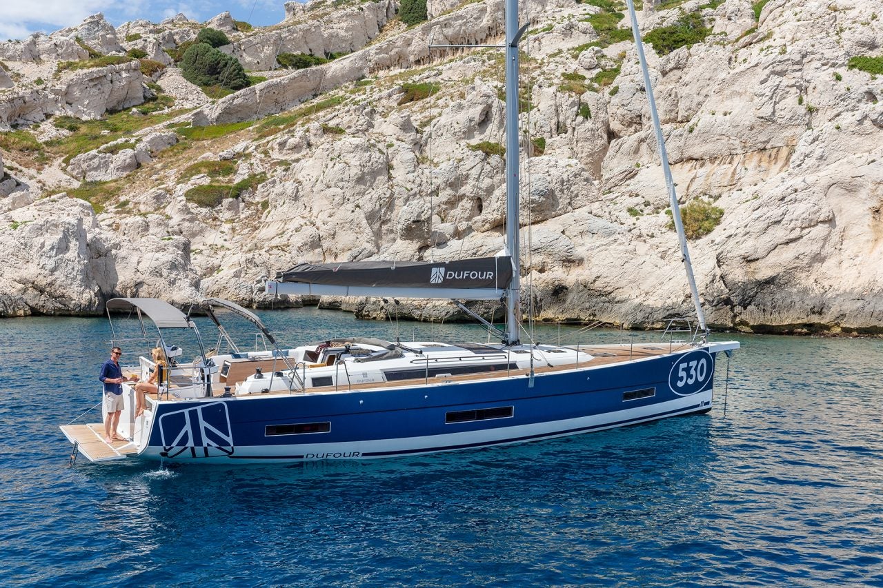 Seitenansicht des vor Anker liegenden Einrumpfsegelboots Dufour 530 mit Paar an Bord